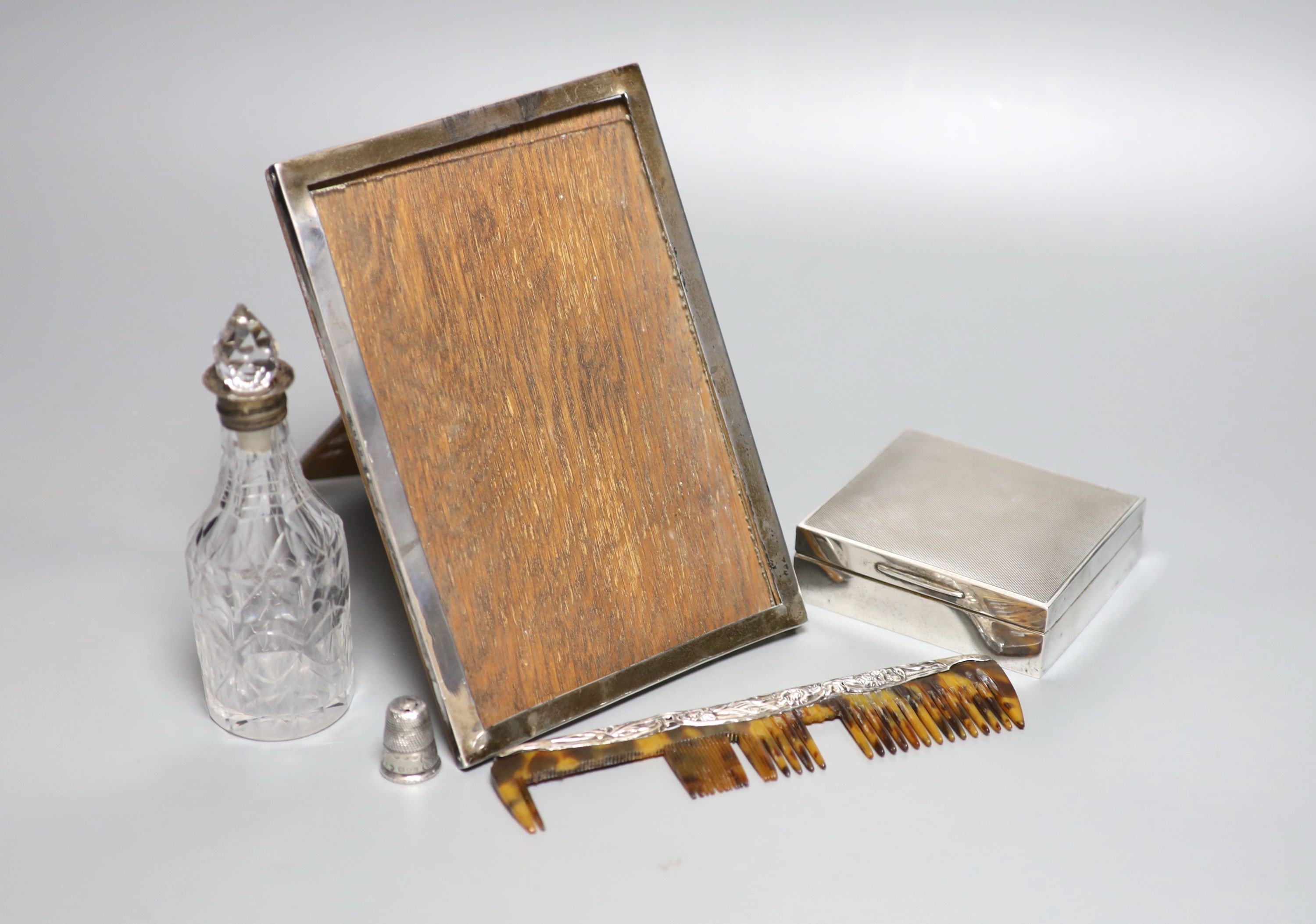 A silver mounted cigarette box, a silver mounted photograph frame, a silver thimble, a silver mounted comb(a.f.) and a silver mounted glass condiment bottle.
